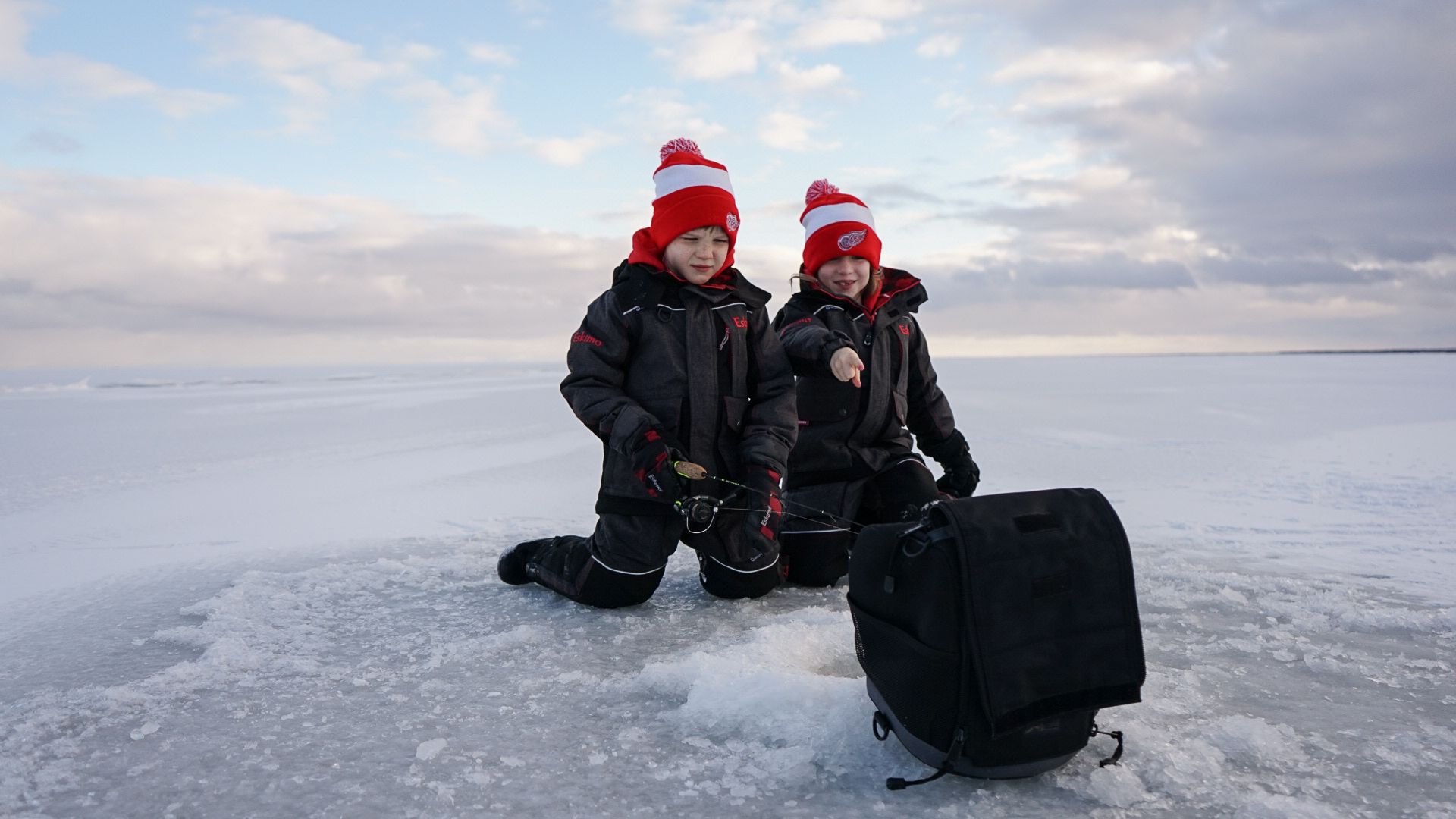Ice fishers sitting on frozen lake with winter gear and fishing equipment.
