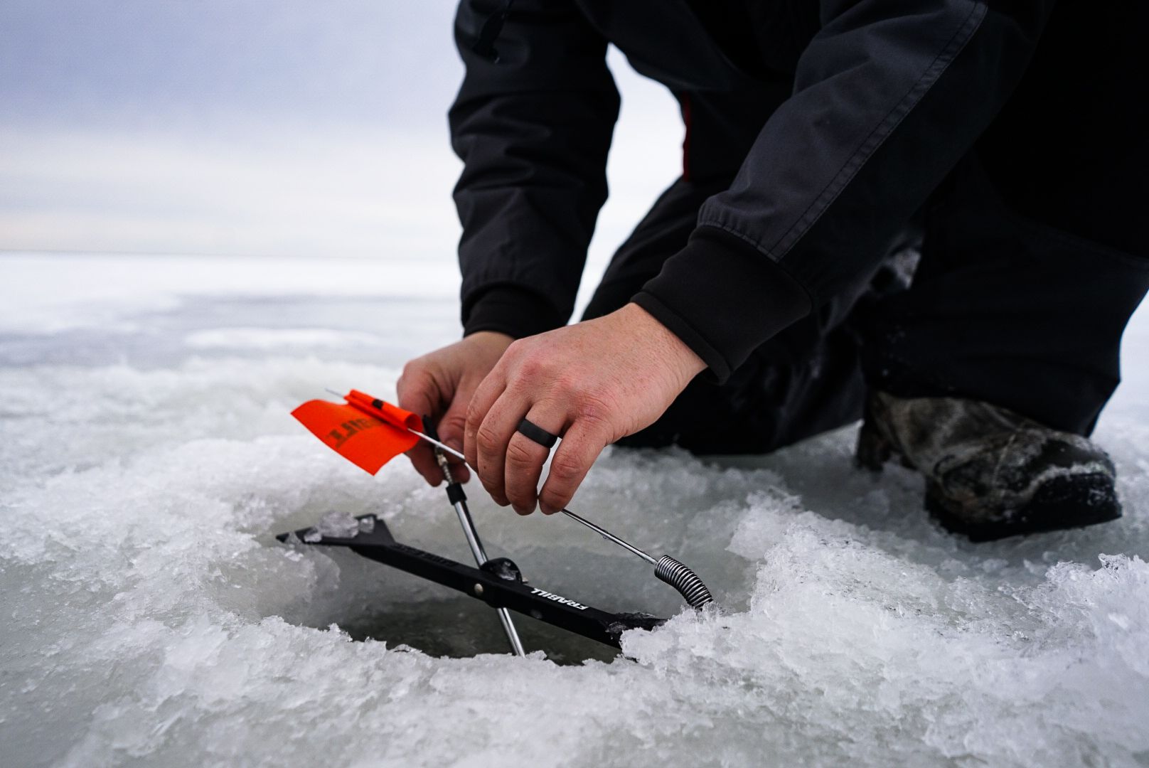 Ice fishing setup with red flag marker on snowy frozen lake surface.