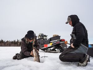 People ice fishing on a snowy lake with their gear spread out on the frozen surface.