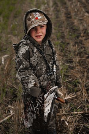 Hunter in camouflage gear positioned in outdoor hunting terrain.