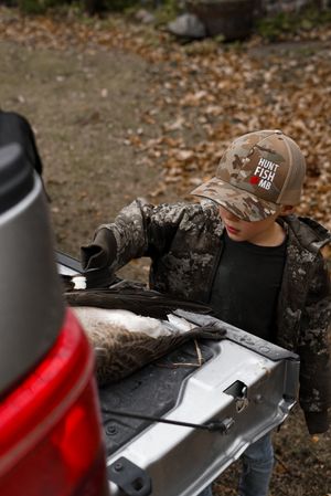Hunter examining a silver surface outdoors in camouflage gear and brown cap.