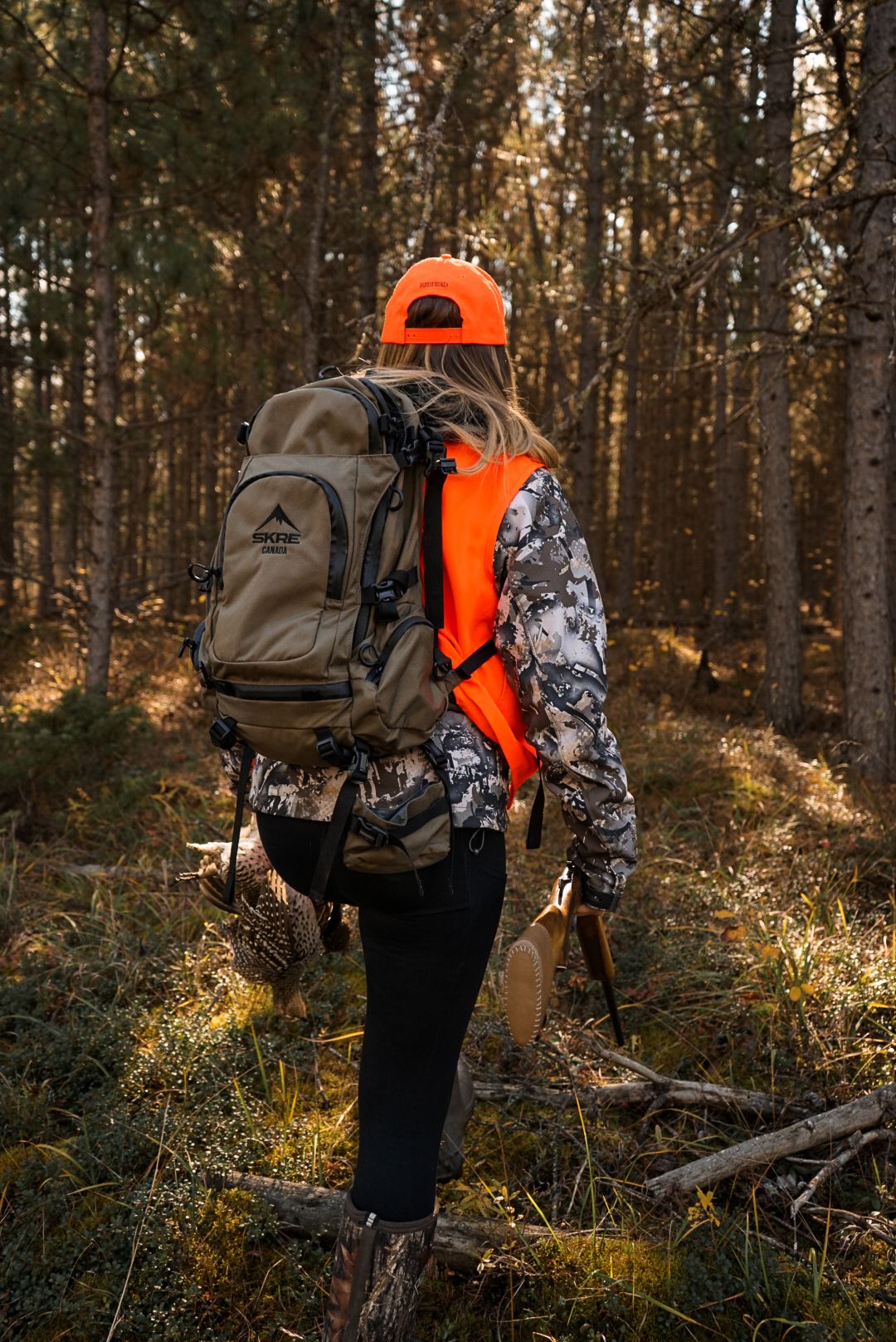 Hunters walking through forest wearing orange safety gear and camouflage backpacks.