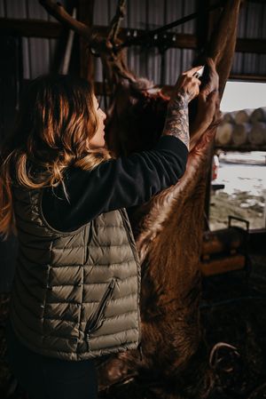 Person in puffy vest examining hanging game meat in dark setting.