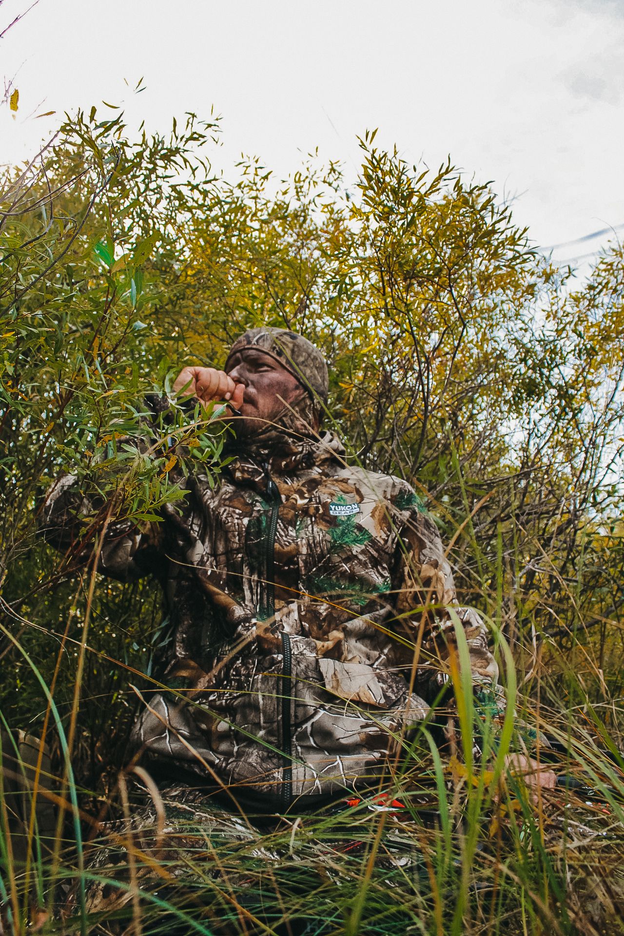 Hunters in camouflage gear positioned among bushes and tall grass.