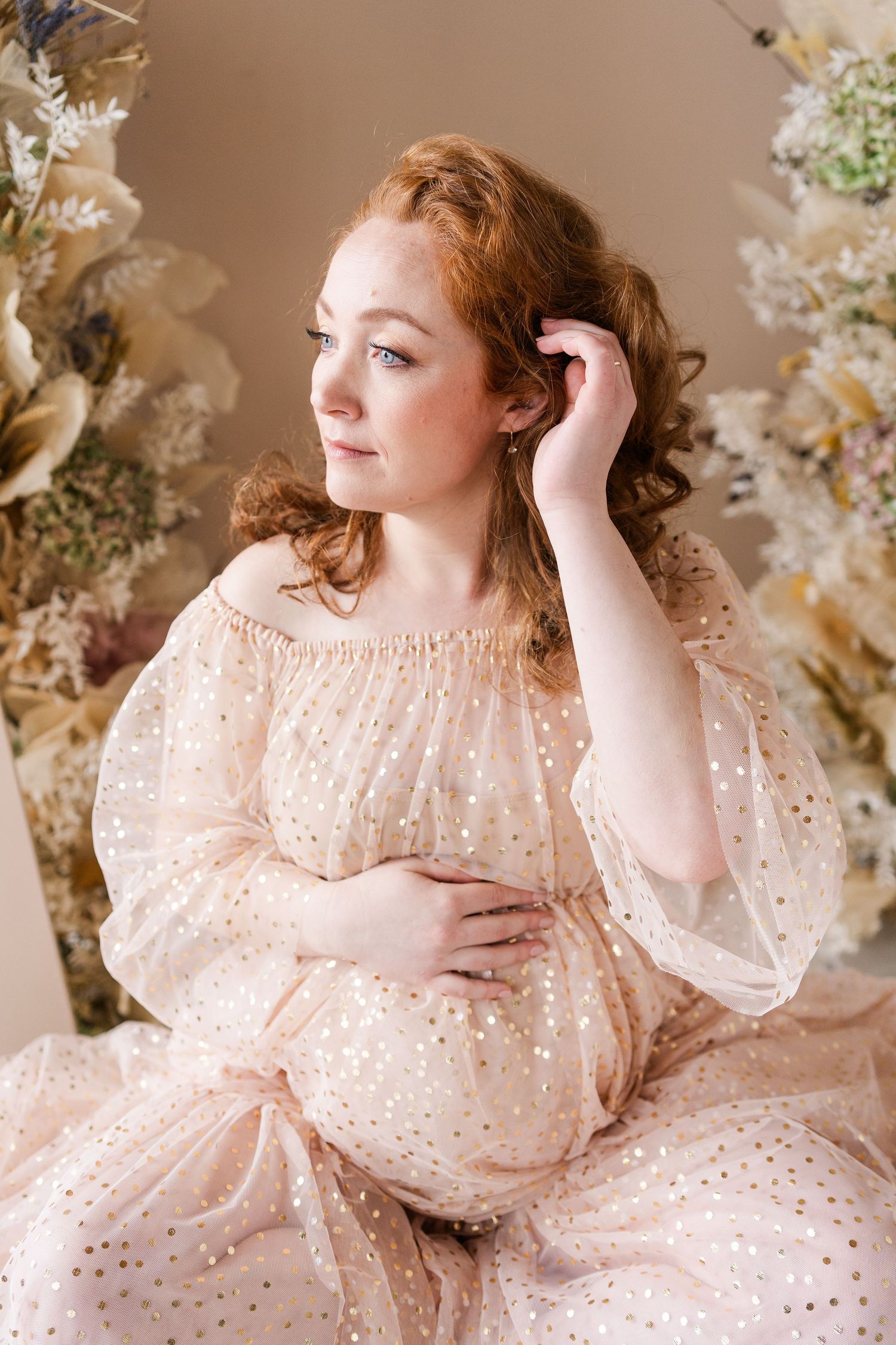 Dreamy maternity portrait in sparkly champagne dress with floral backdrop and soft lighting.