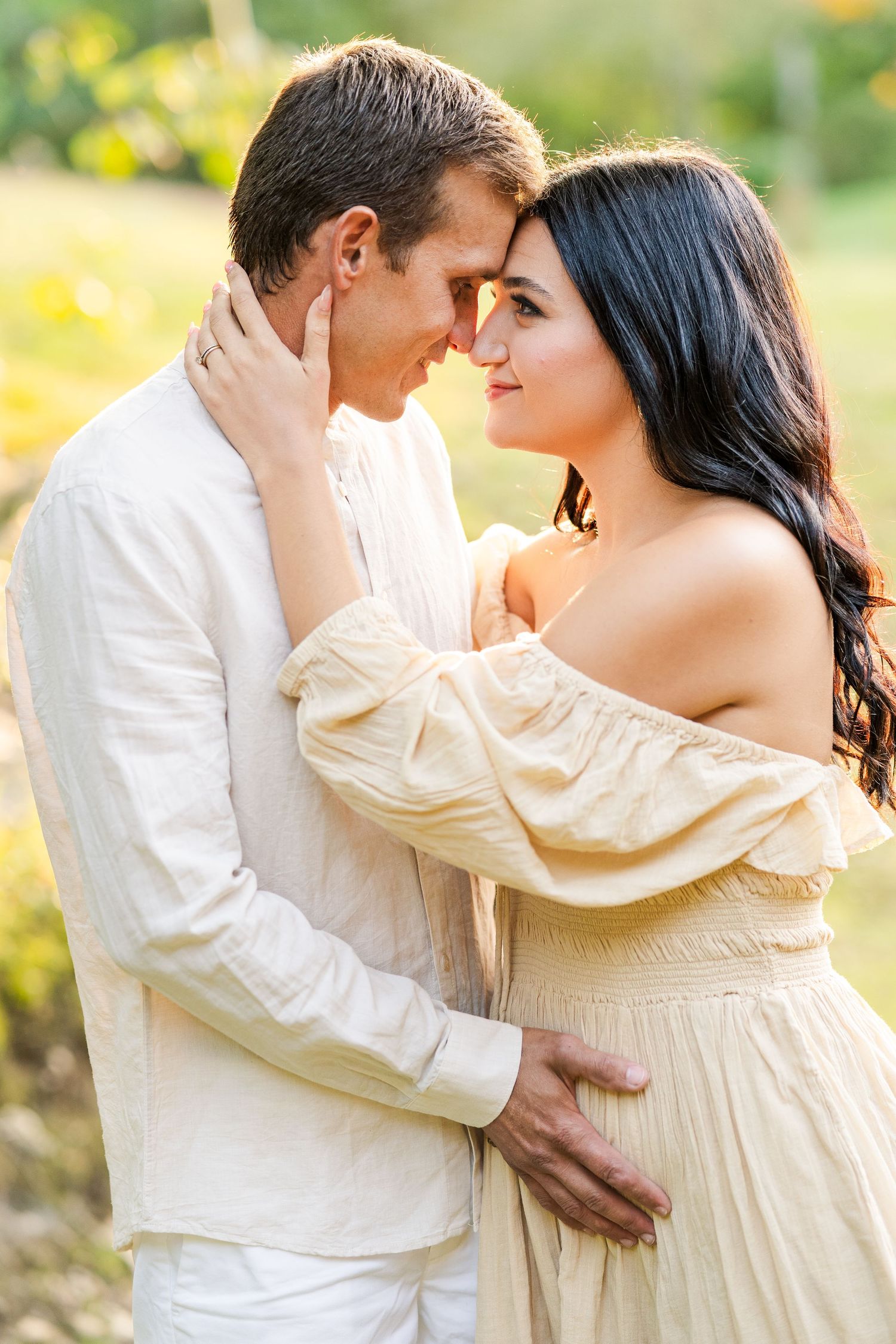 Intimate portrait of couple in white and cream outfits sharing tender moment in golden sunlight.