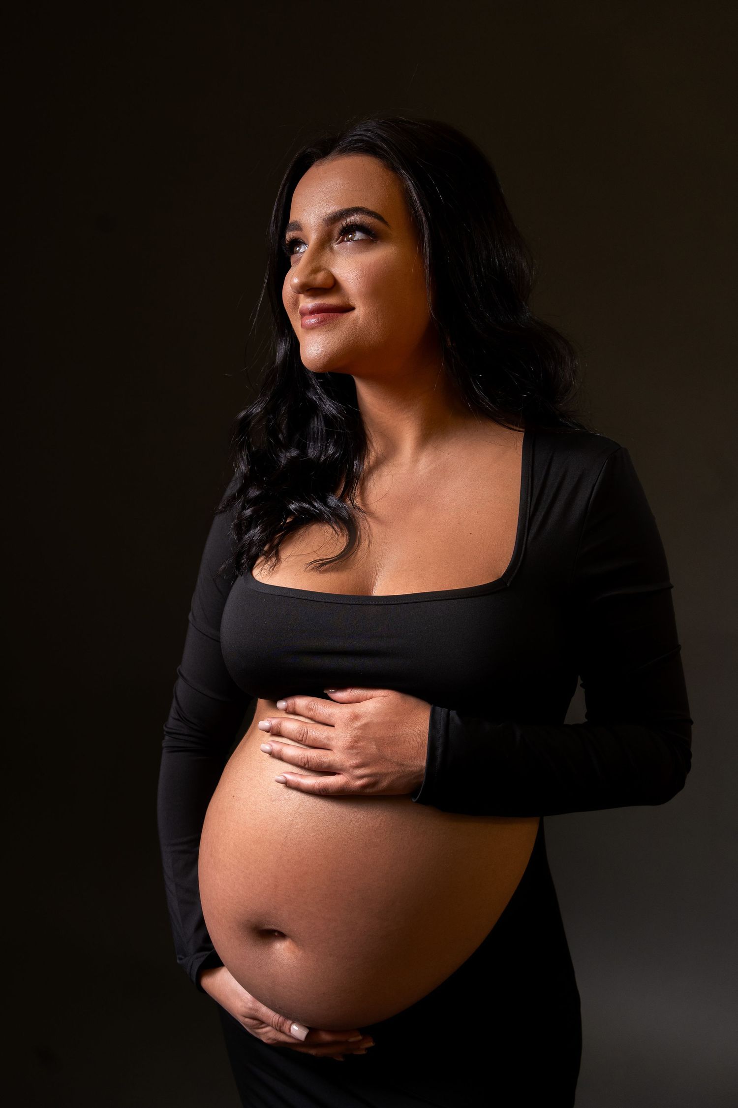 Maternity portrait featuring a woman in black dress against dark background.