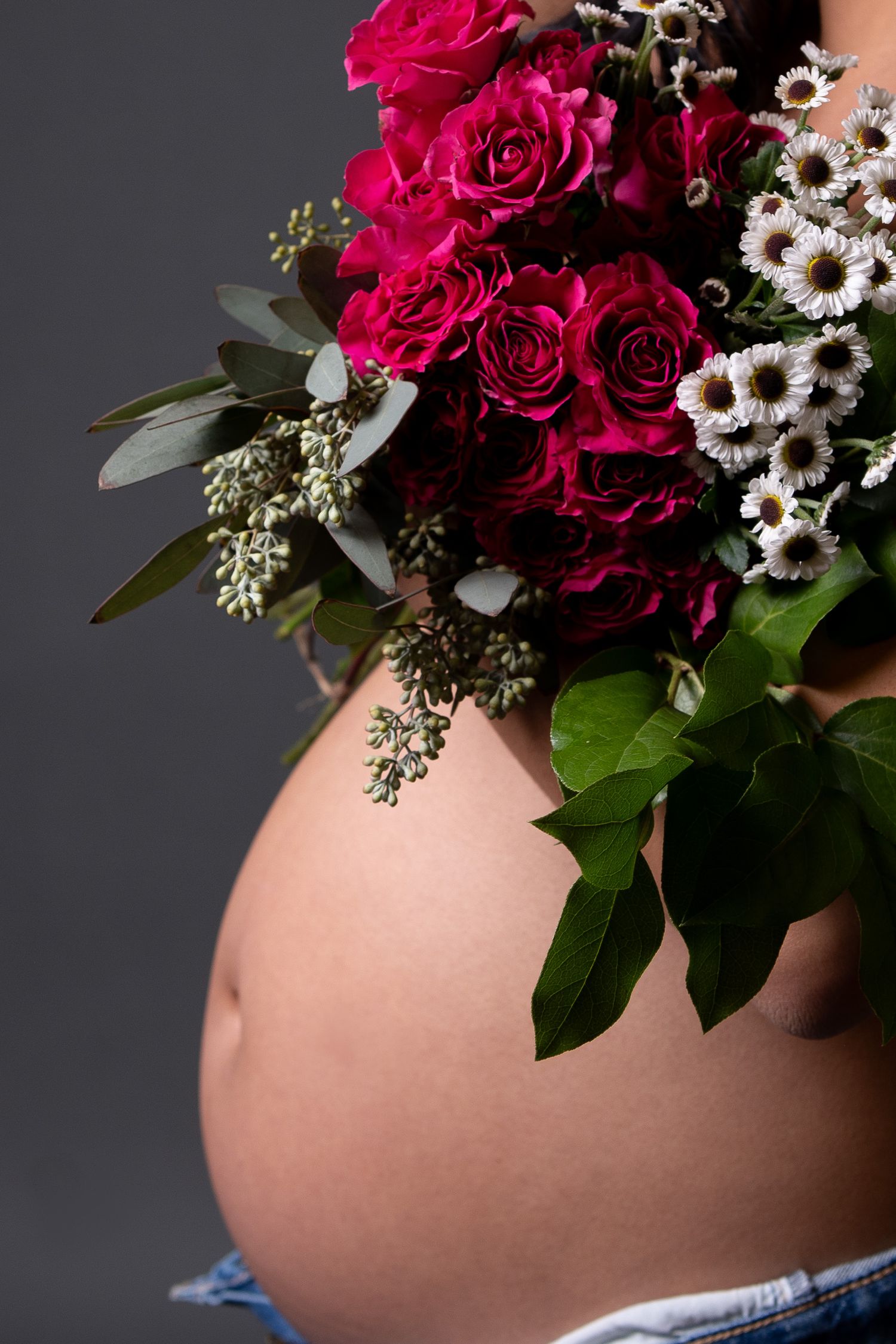 Artistic maternity photo with bright red roses against pregnant belly.
