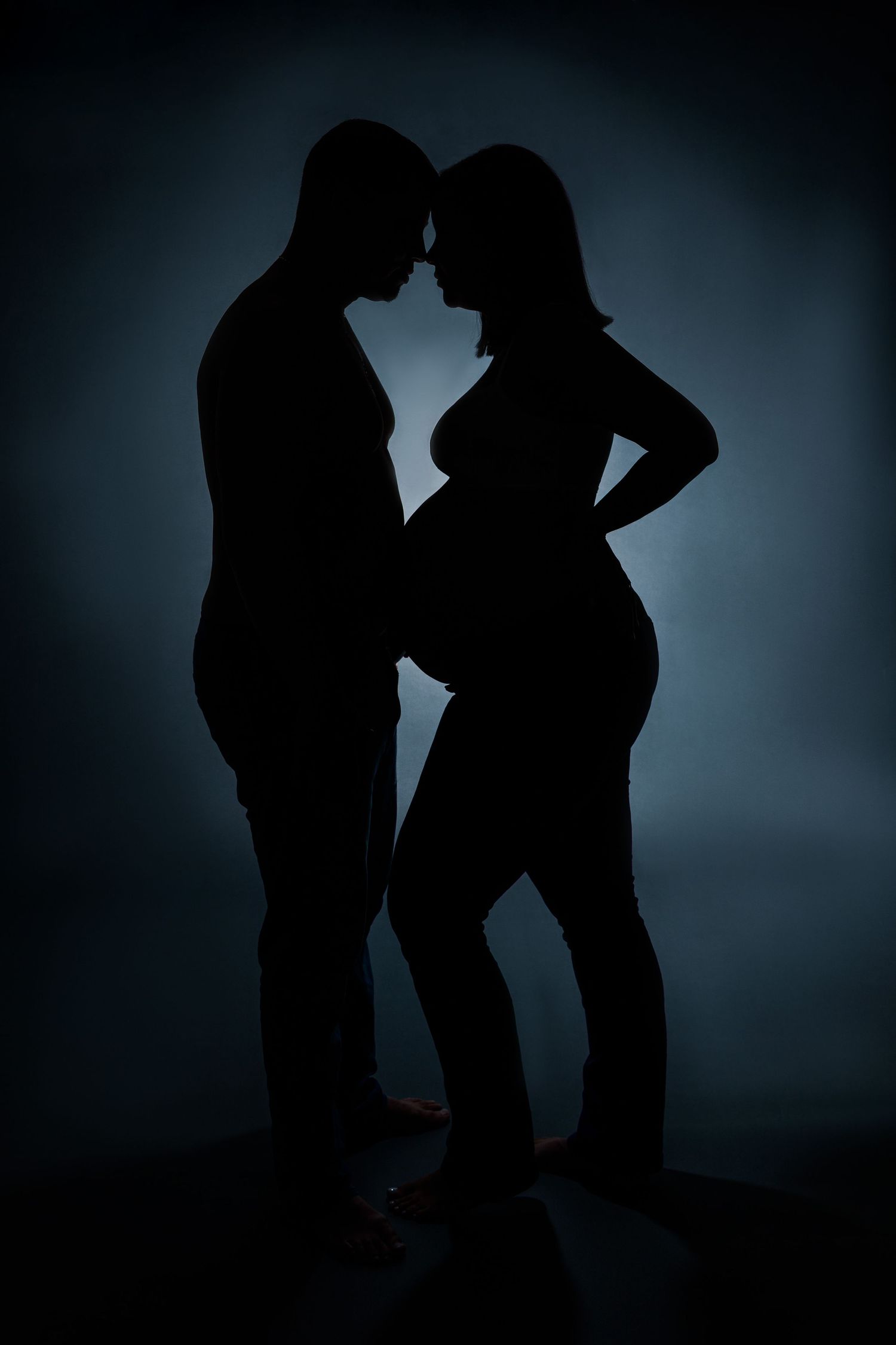 Silhouette of expectant couple facing each other against blue background.