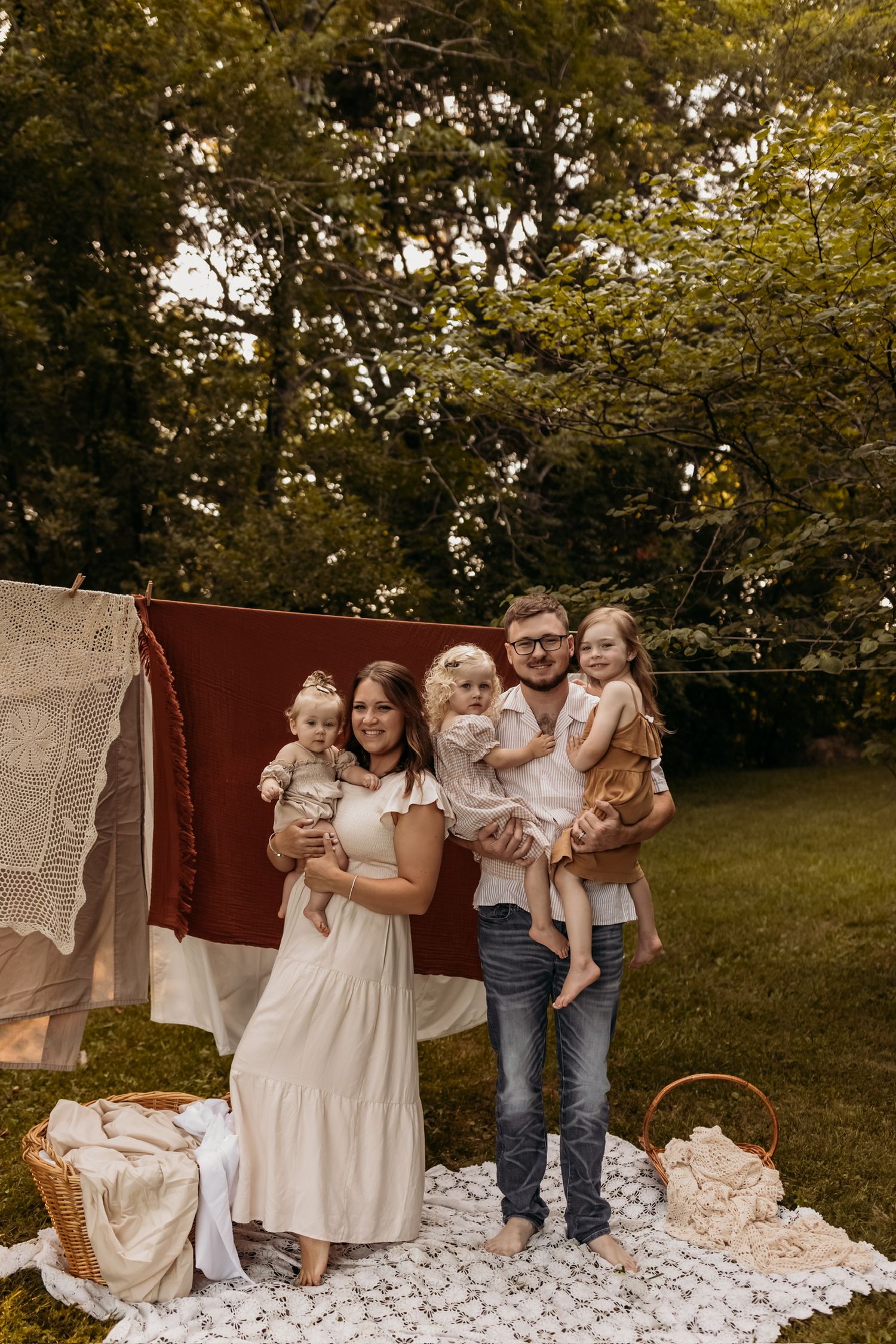 Family of five posing together outdoors against rustic backdrop with hanging linens.