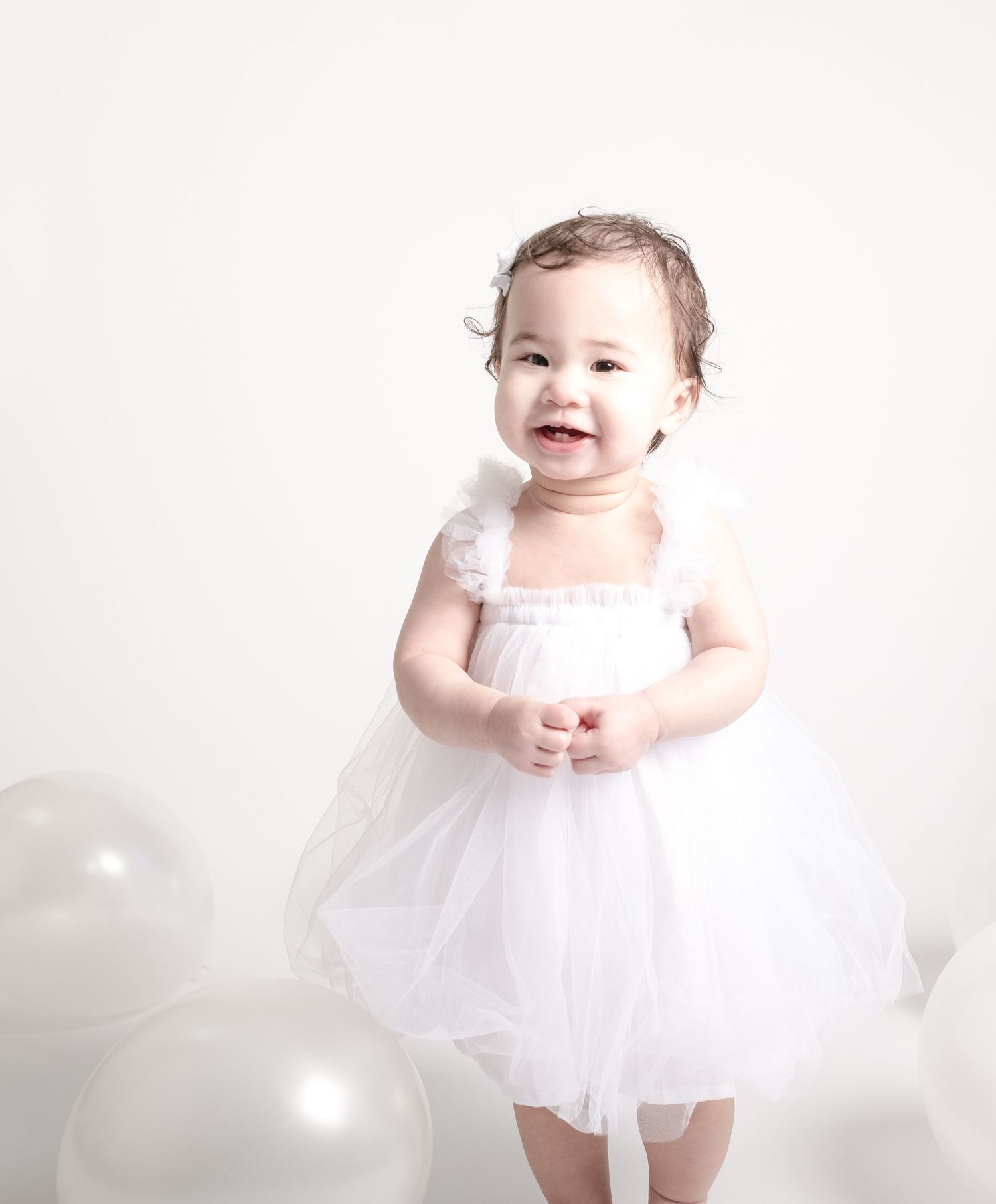 Baby in white tutu dress against bright white background.