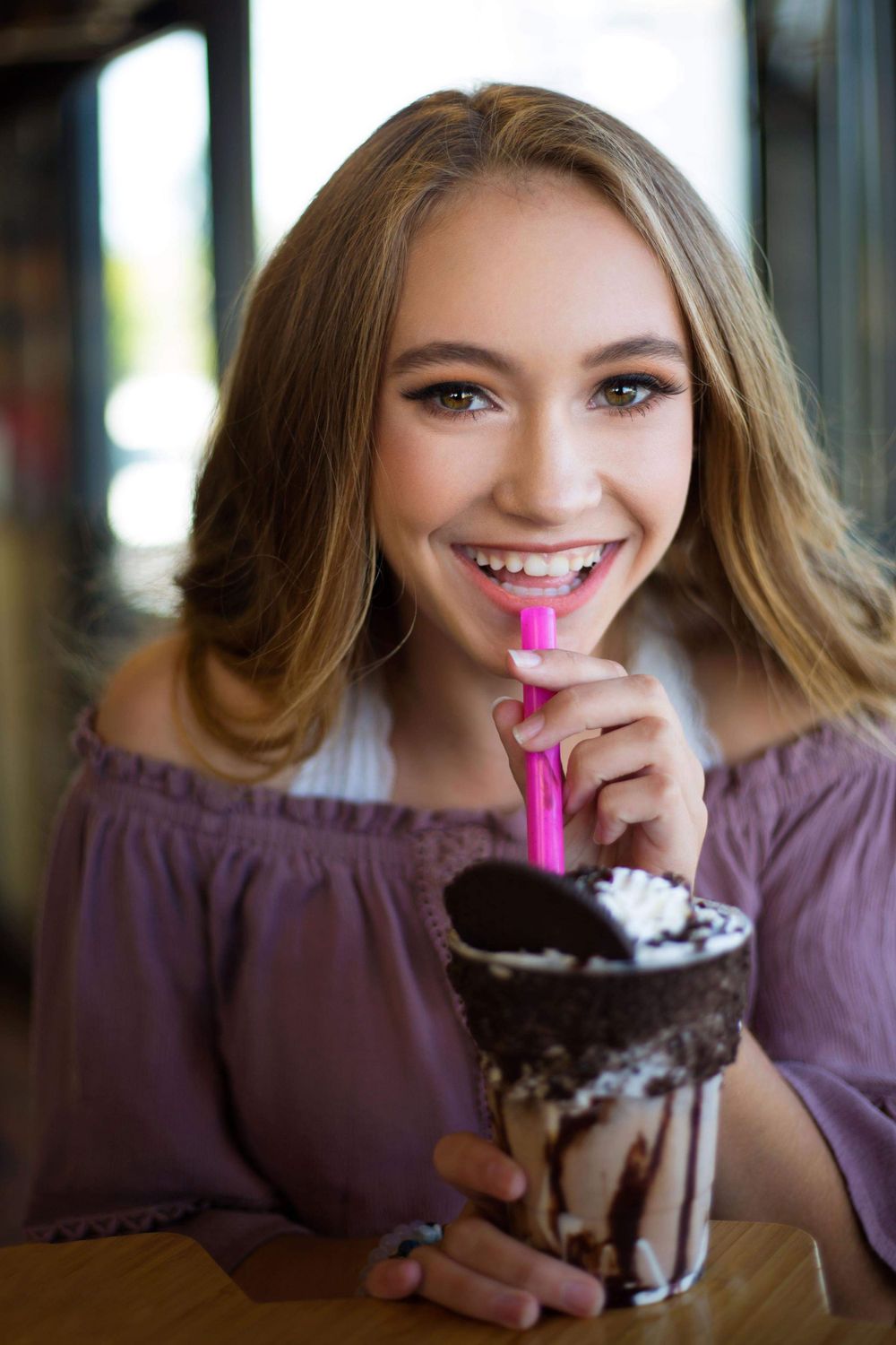 Someone enjoying a decadent chocolate milkshake topped with whipped cream while wearing a purple off-shoulder top.
