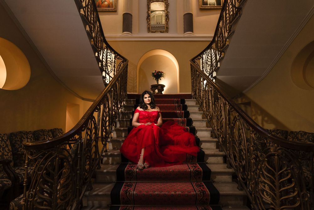 Elegant staircase photoshoot featuring a red gown against ornate wrought iron railings in a historic setting.