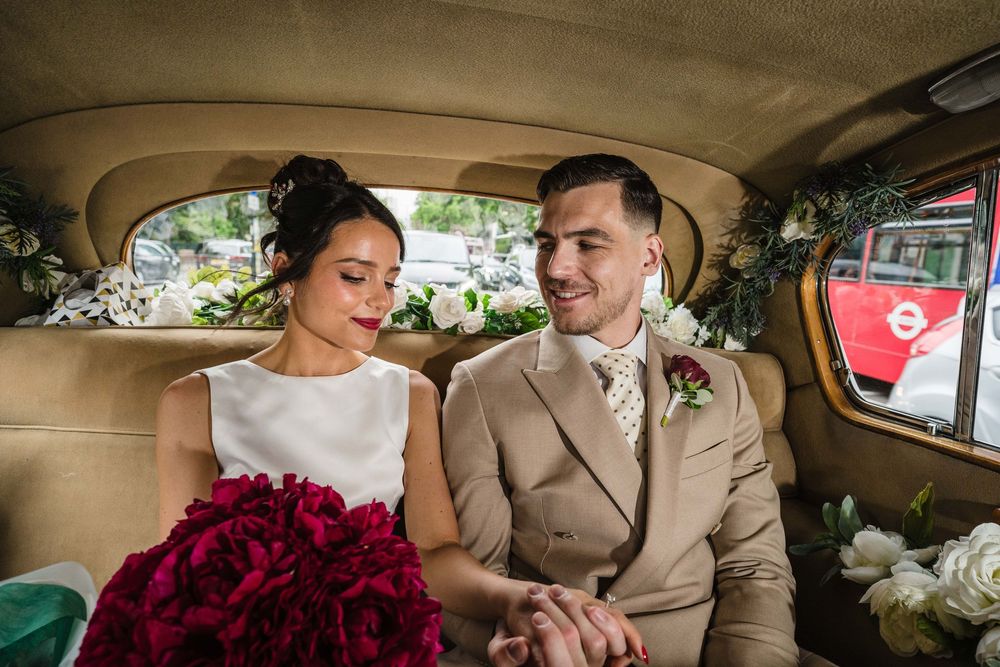 A couple in wedding attire share a moment in the back of a vintage car with deep red roses.