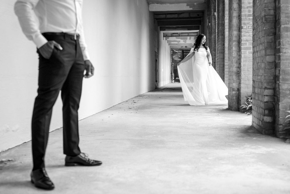 Black and white photo showing a long elegant corridor with a bride and groom standing at opposite ends.