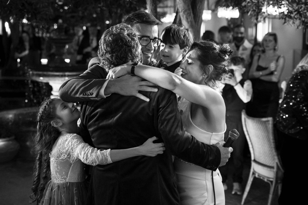 A tender black and white moment captured during a wedding dance as guests embrace in a group hug on the dance floor.