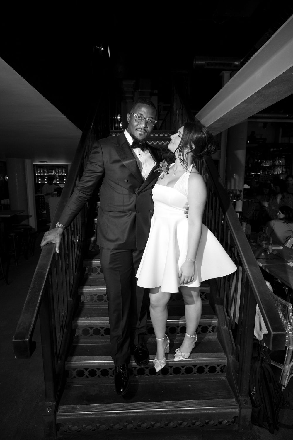 Black and white photos of a couple descending stairs in formal attire during a special occasion.