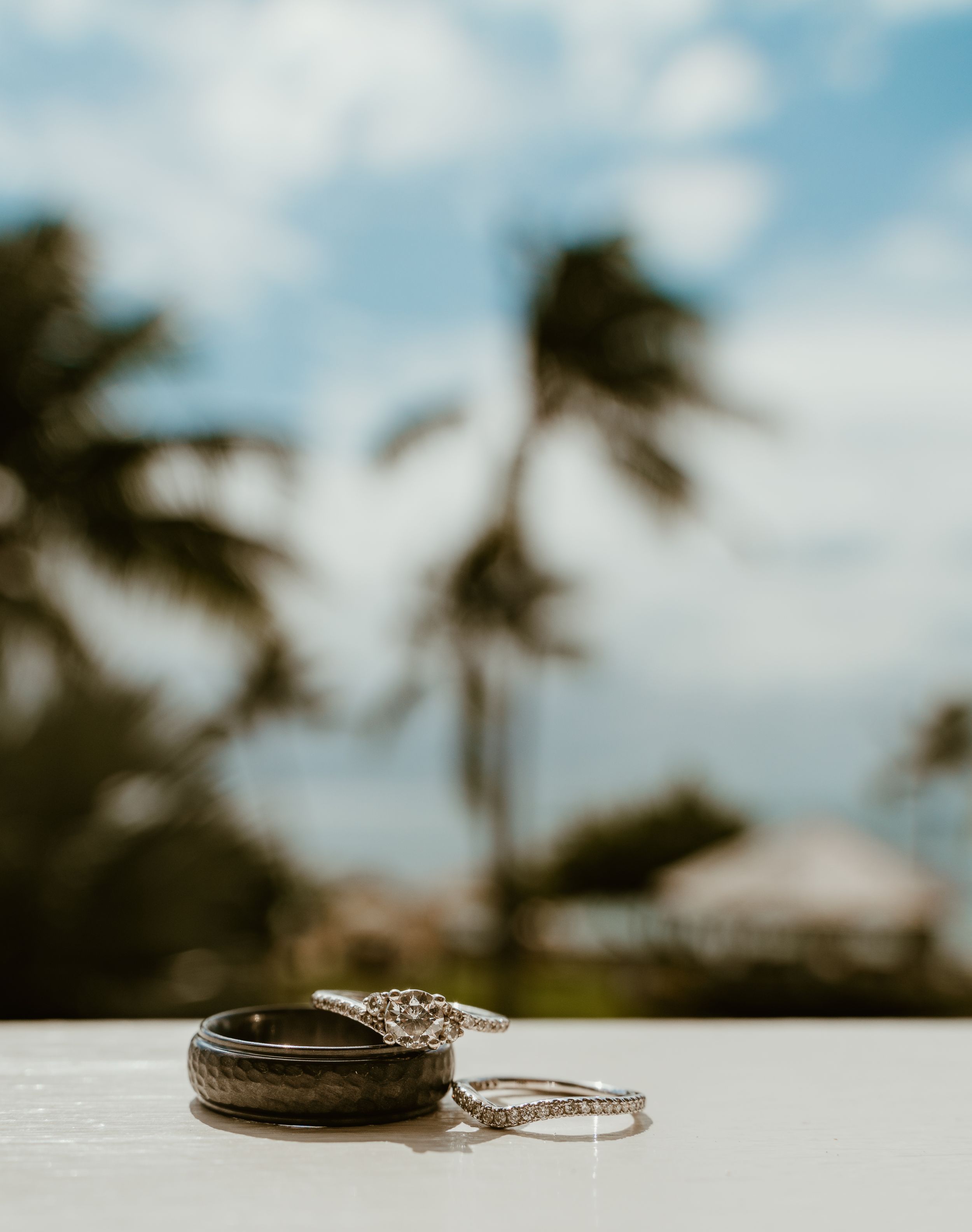 Wedding rings resting on a white surface with palm trees and blue sky in the background.