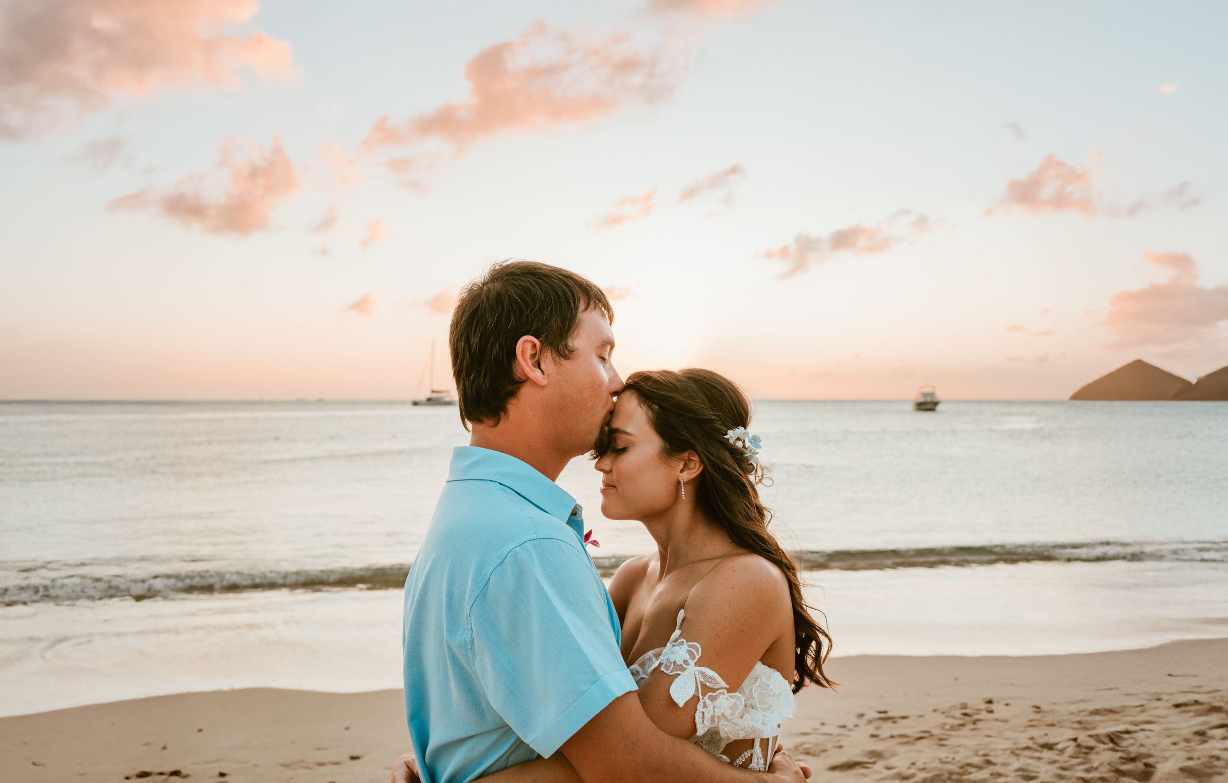 Romantic couple embracing on a Hawaiian beach at sunset with a mountain island in the background.