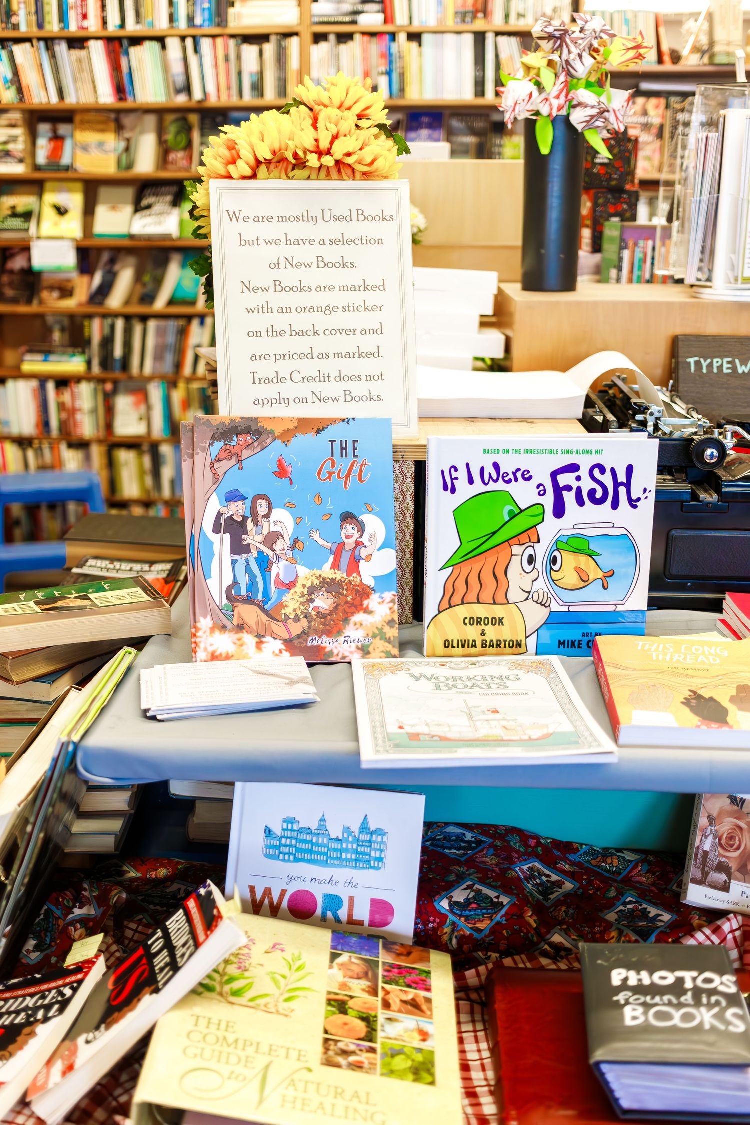 A bookstore display table featuring children's books and a sign among scattered merchandise.
