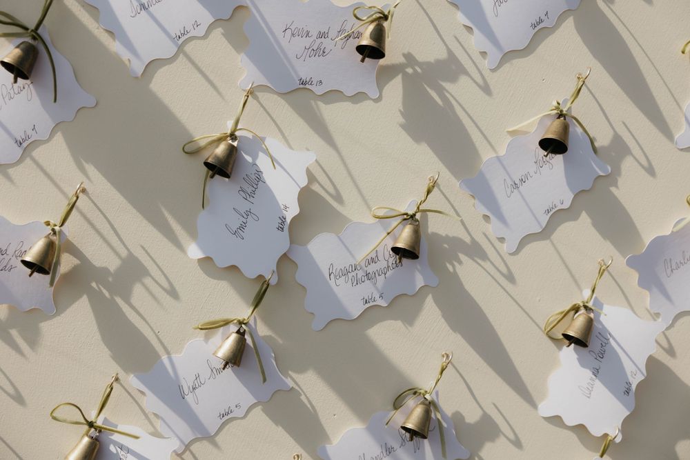 Wedding seating chart cards with gold bells attached displayed on a cream background.