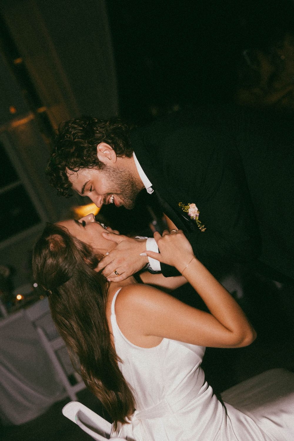 Bride and groom sharing romantic first dance kiss at dimly lit wedding reception.