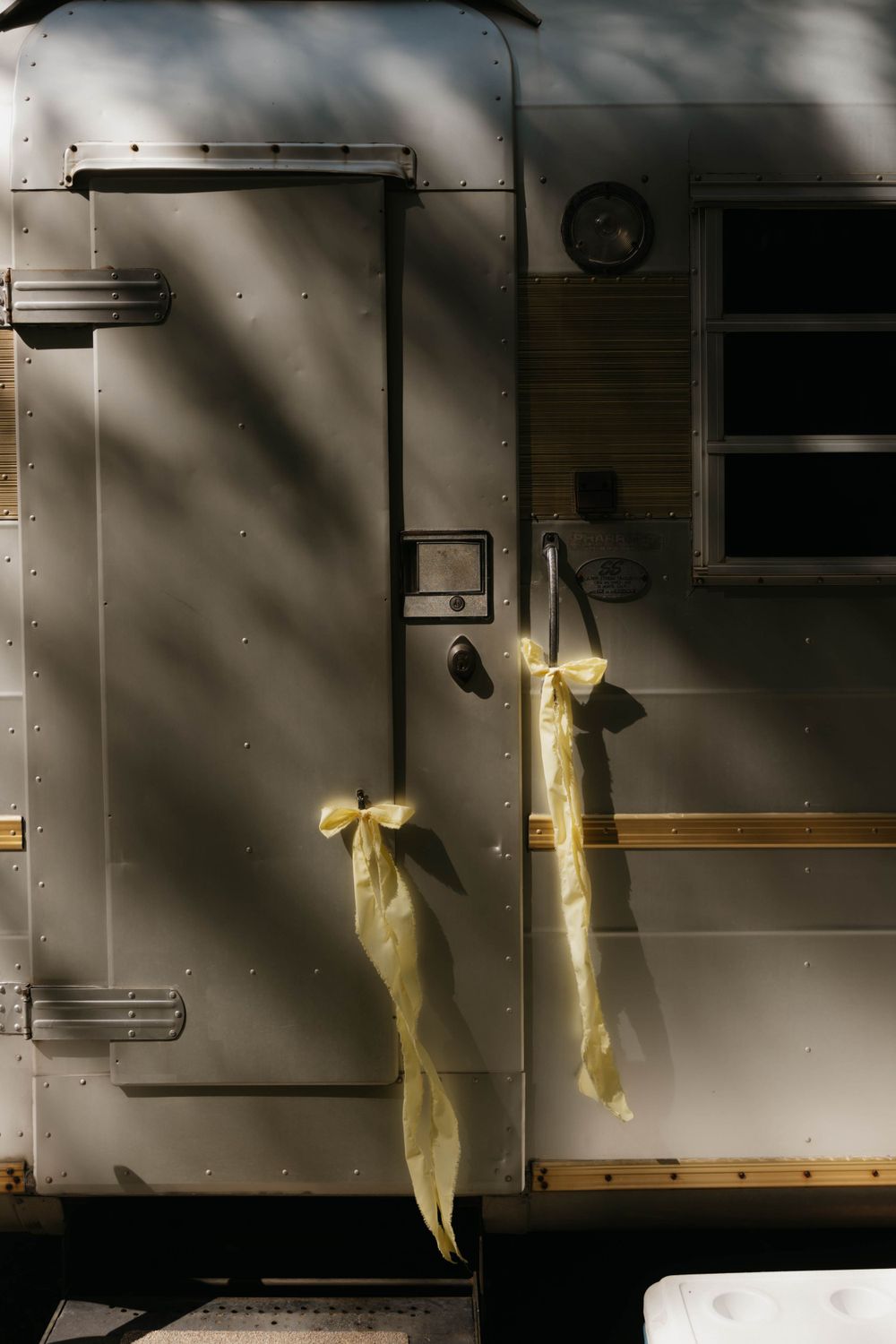 Close-up of vintage silver Airstream trailer door decorated with yellow ribbon bows for outdoor wedding.