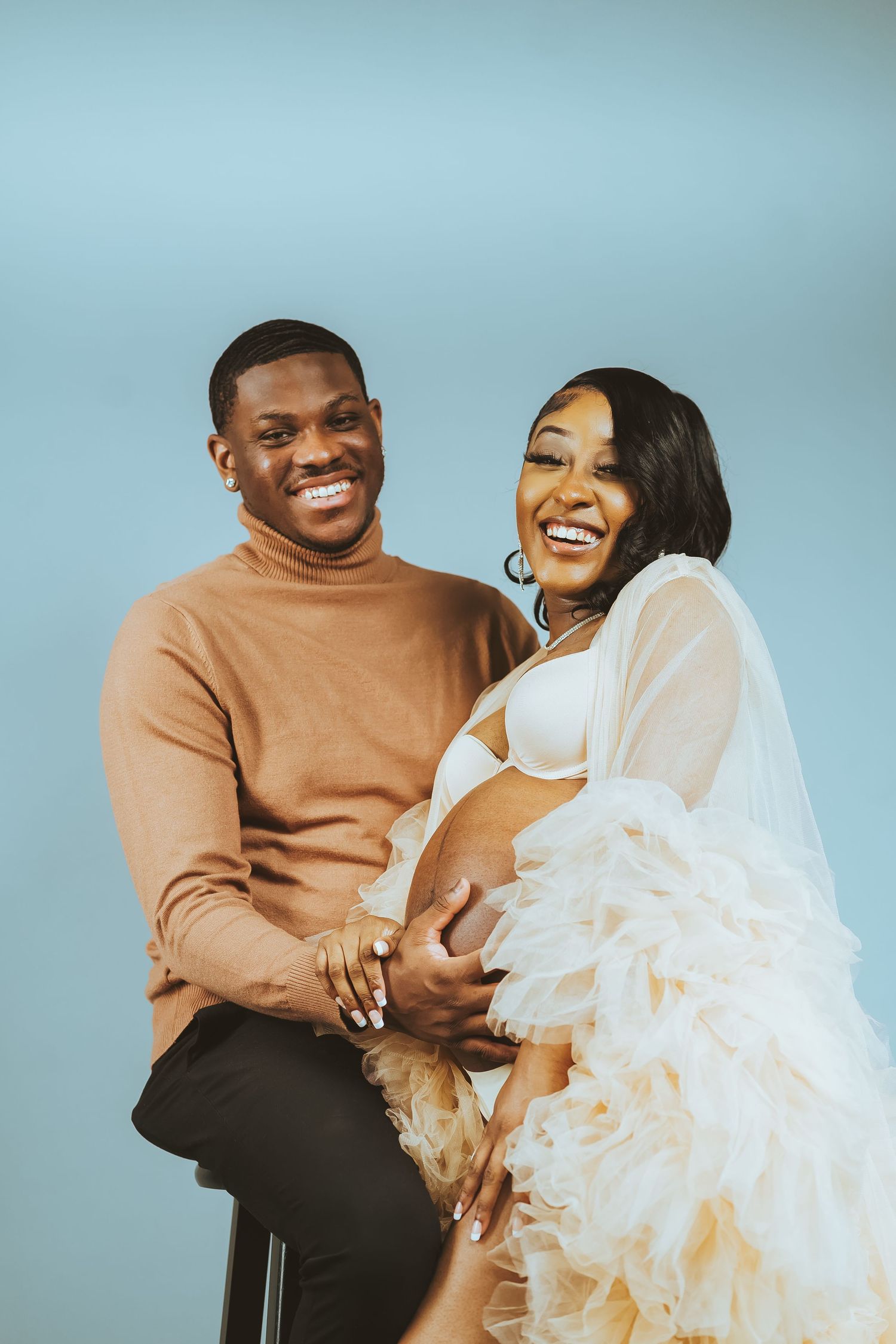 Couple sharing a joyful moment during a romantic photoshoot against light blue background.