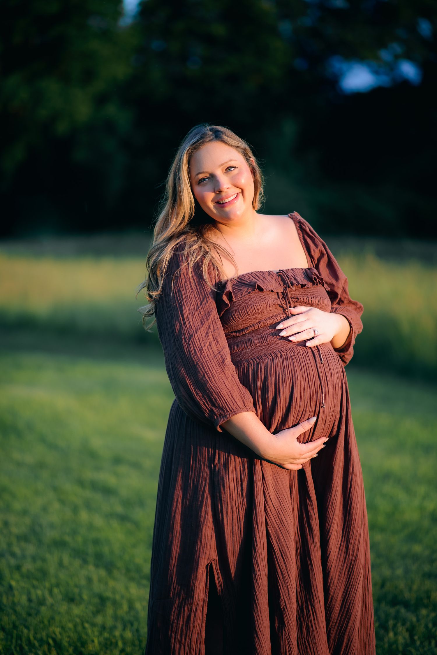 pregnant mother in flowing dress standing in golden light during outdoor maternity session