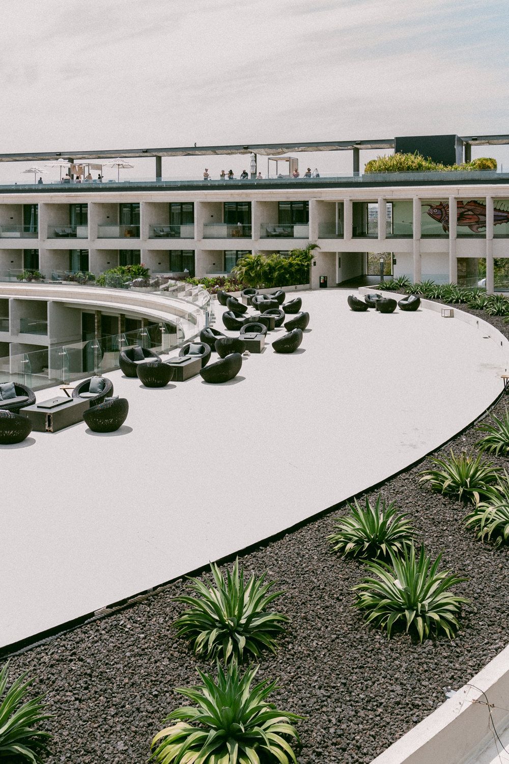 Modern curved hotel building with outdoor lounge furniture and tropical landscaping.