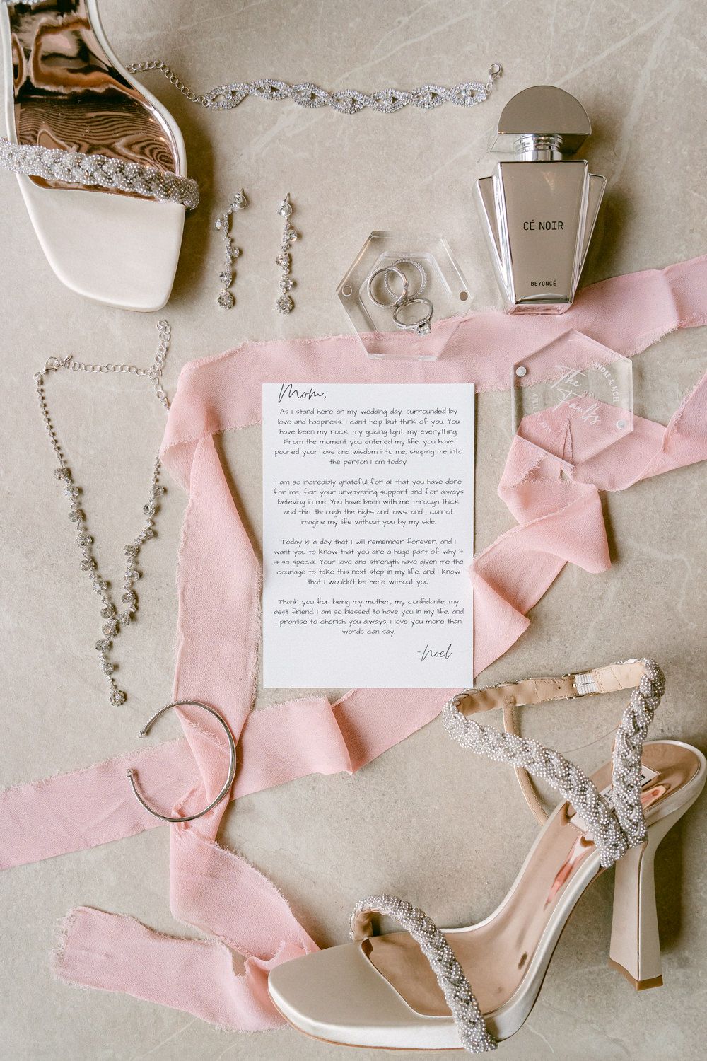Wedding accessories including jewelry, shoes, perfume and a letter arranged on pink ribbon.
