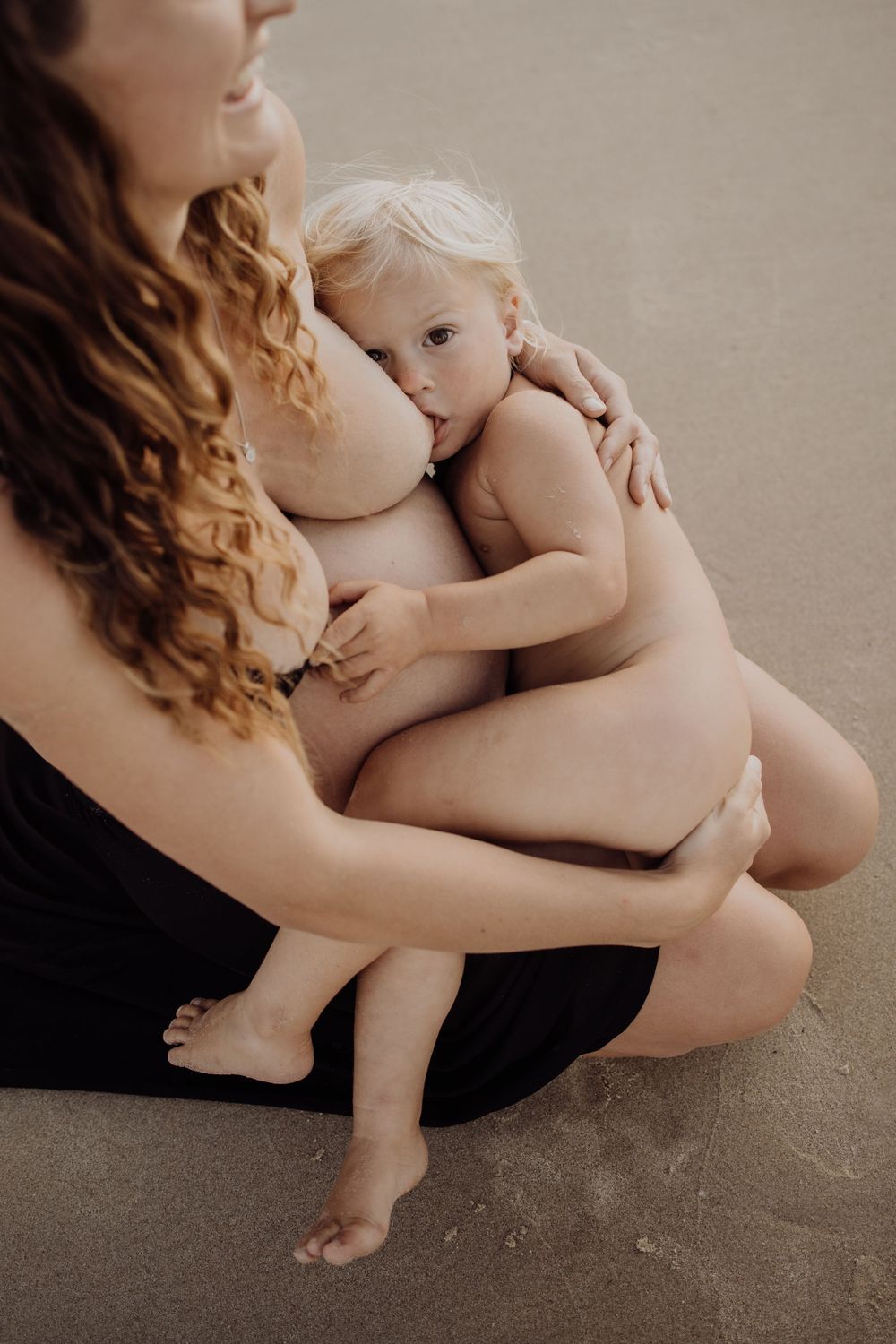 Expectant mother breastfeeding her first born child during a natural sunset maternity photography session at Maslin Beach, South Australia