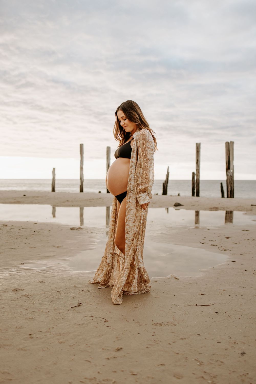 Expecting mum standing amongst the jetty ruins during a natural sunset pregnancy photography session at Port Willunga, South Australia