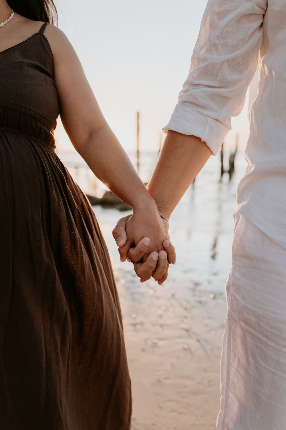 Pregnant mother and partner hold hands while photographed beside the coast during a relaxed maternity session at Port Willunga, Adelaide