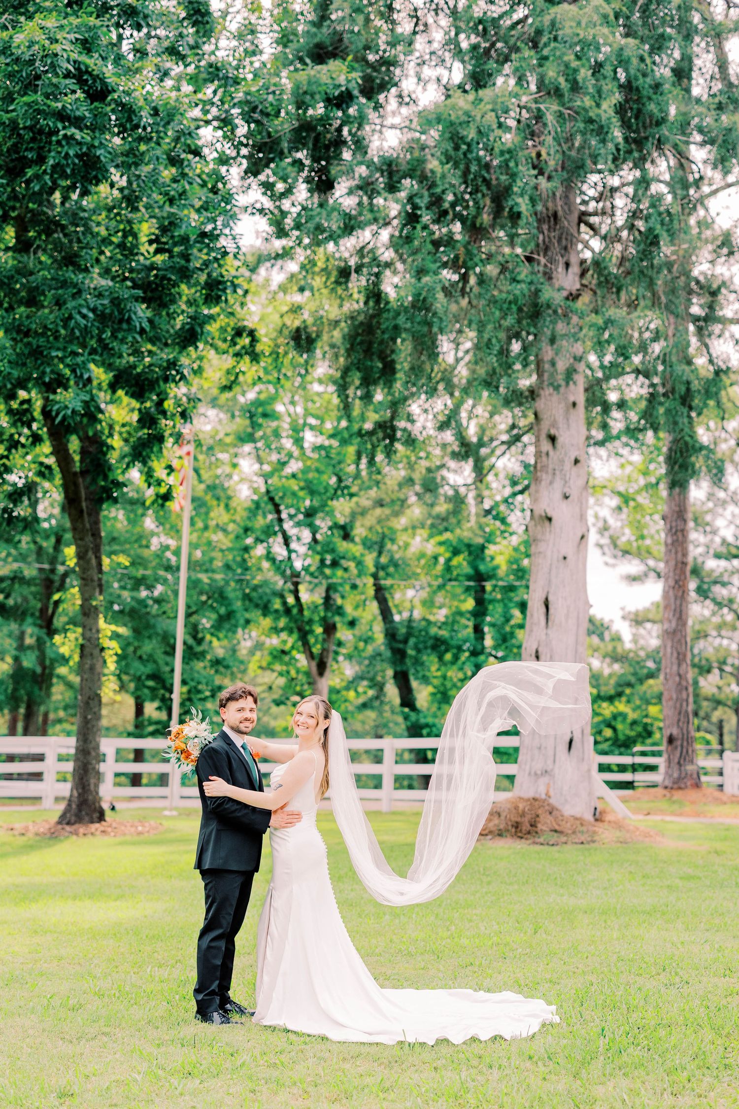 A couple holds hands high on a grassy hilltop during their outdoor wedding celebration with mountain scenery in the background.