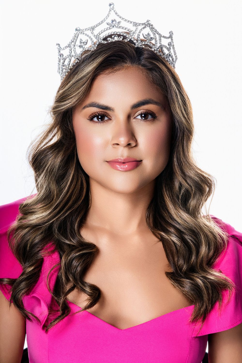 Close-up beauty portrait with crown and pink dress against white backdrop.