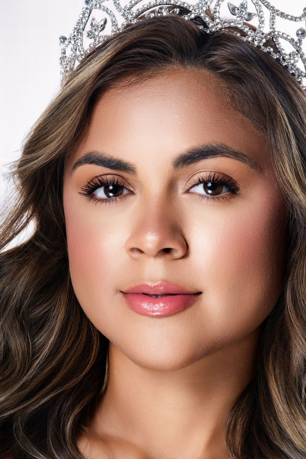 Close-up beauty shot with crown and professional makeup against white background.