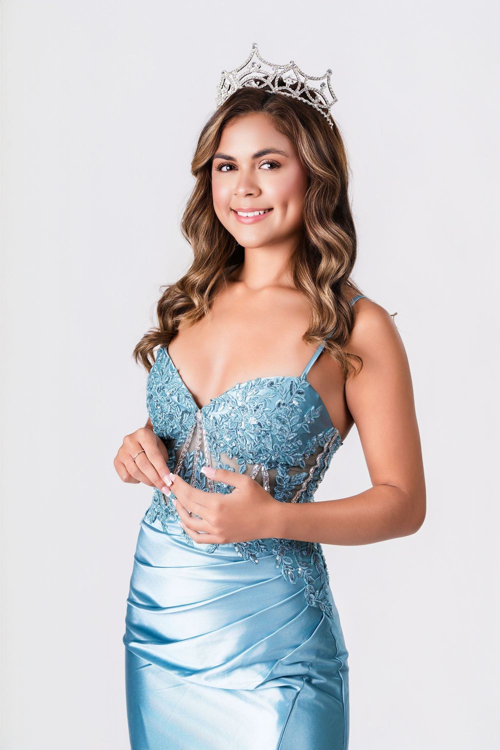 Beauty queen wearing sparkly blue formal dress and tiara poses in studio setting.