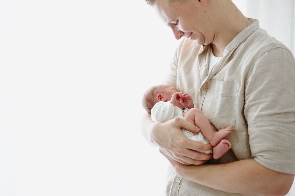 A parent tenderly holds a newborn baby against their chest in soft natural light.