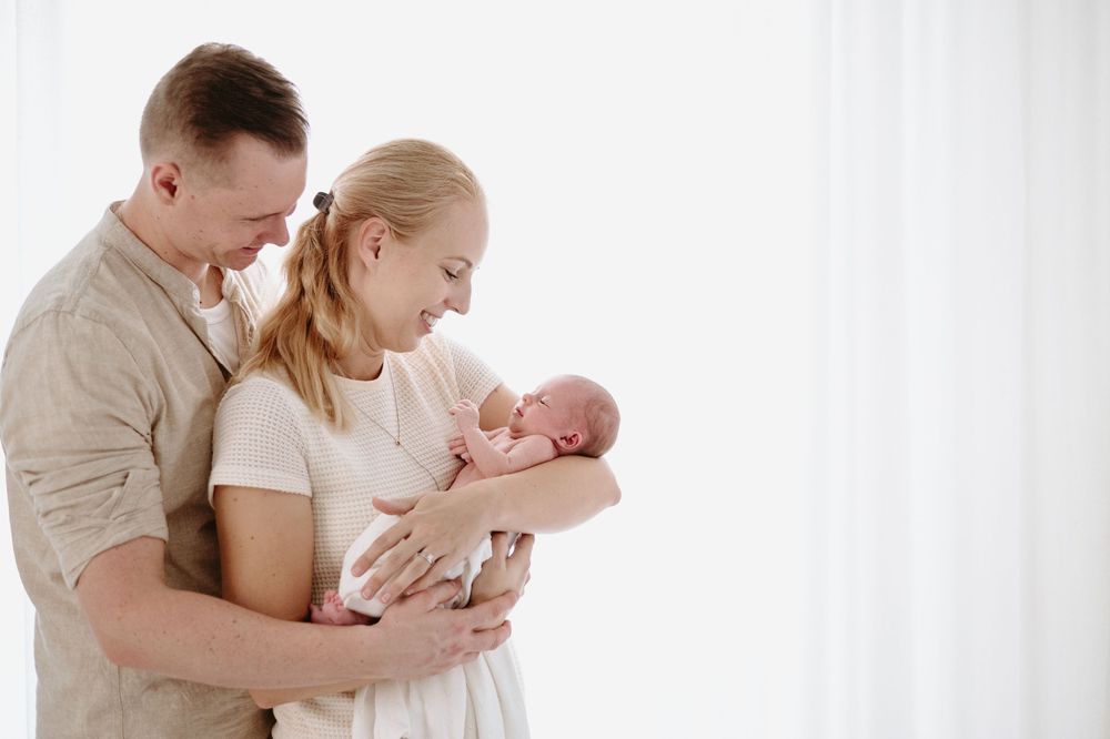 A couple tenderly holds their newborn baby in a bright, white studio setting.