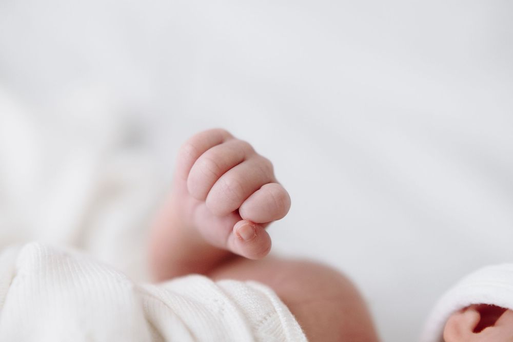 Close-up of a newborn baby's tiny hand with delicate fingers resting on a soft white blanket.