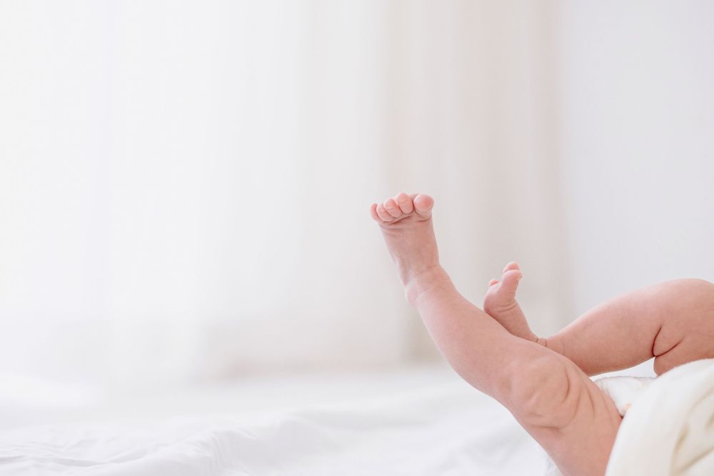 Newborn baby legs raised up on white bedding in a bright, airy room.