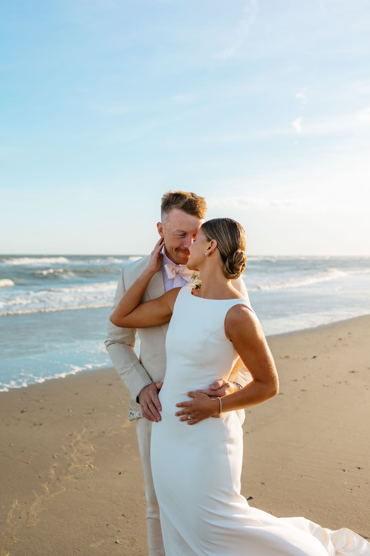 A romantic moment between newlyweds on a sunlit beach with ocean waves in the background.