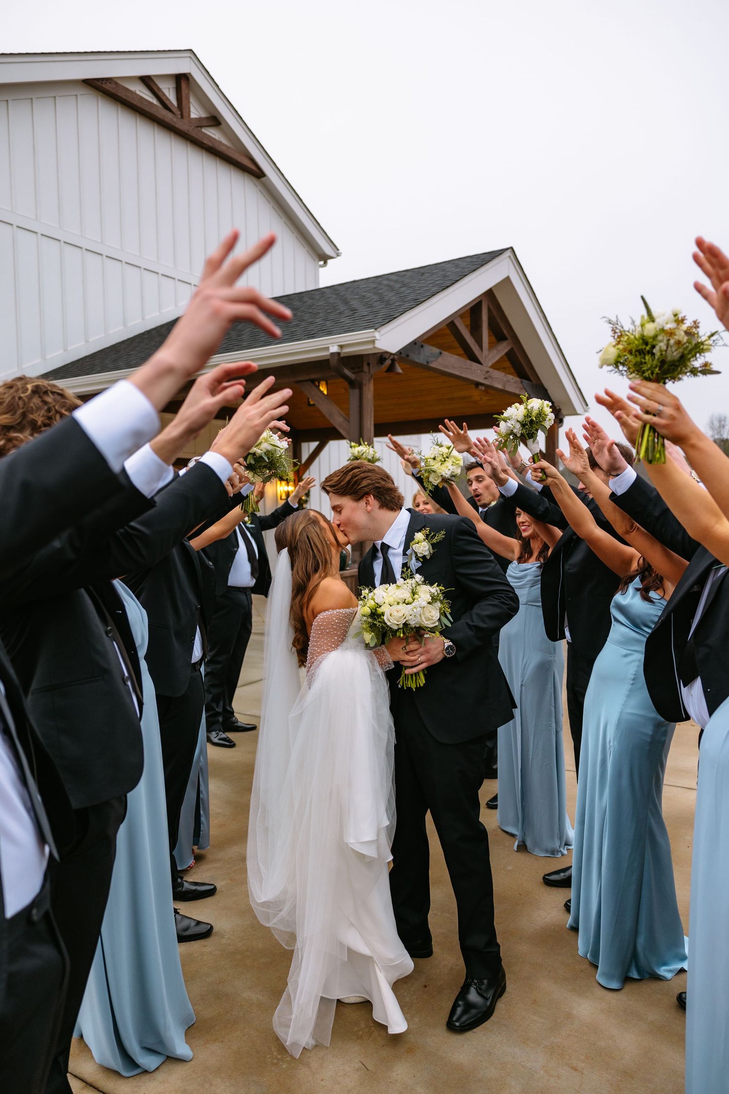 Wedding celebration with bridesmaids in blue dresses and groomsmen creating an arch tunnel for the newlyweds.
