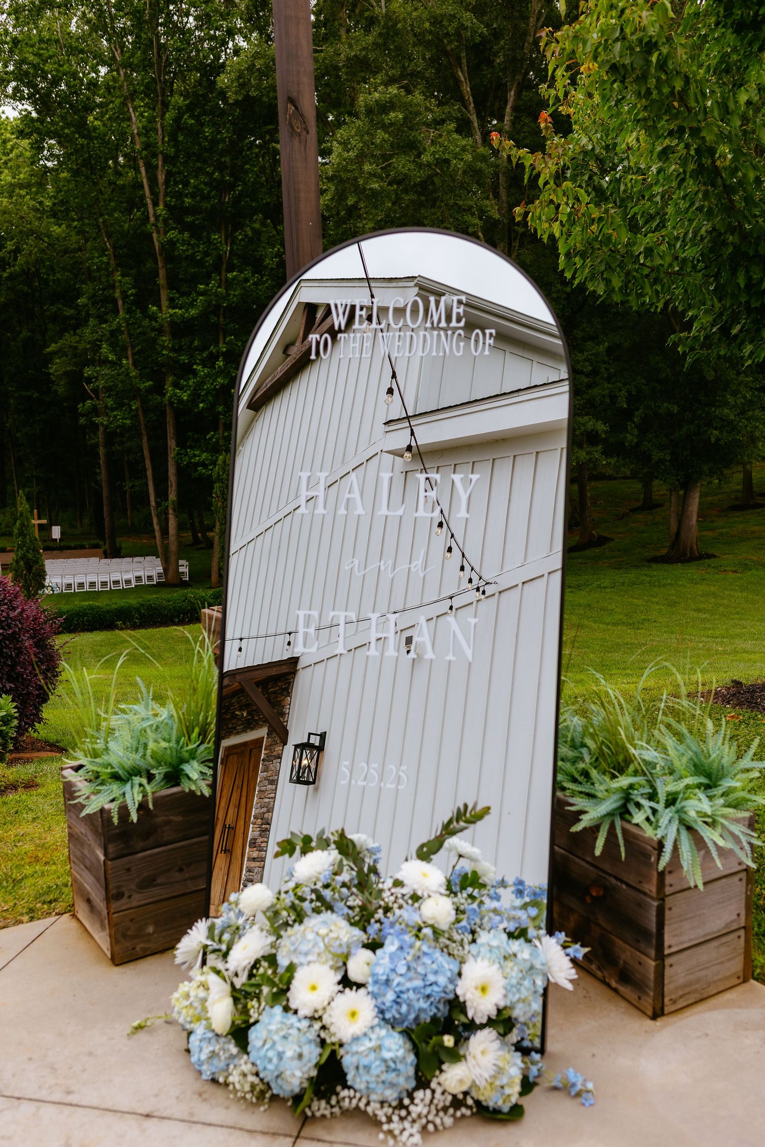 White decorative welcome sign with rustic wooden planters and blue and white hydrangea floral arrangement at base.
