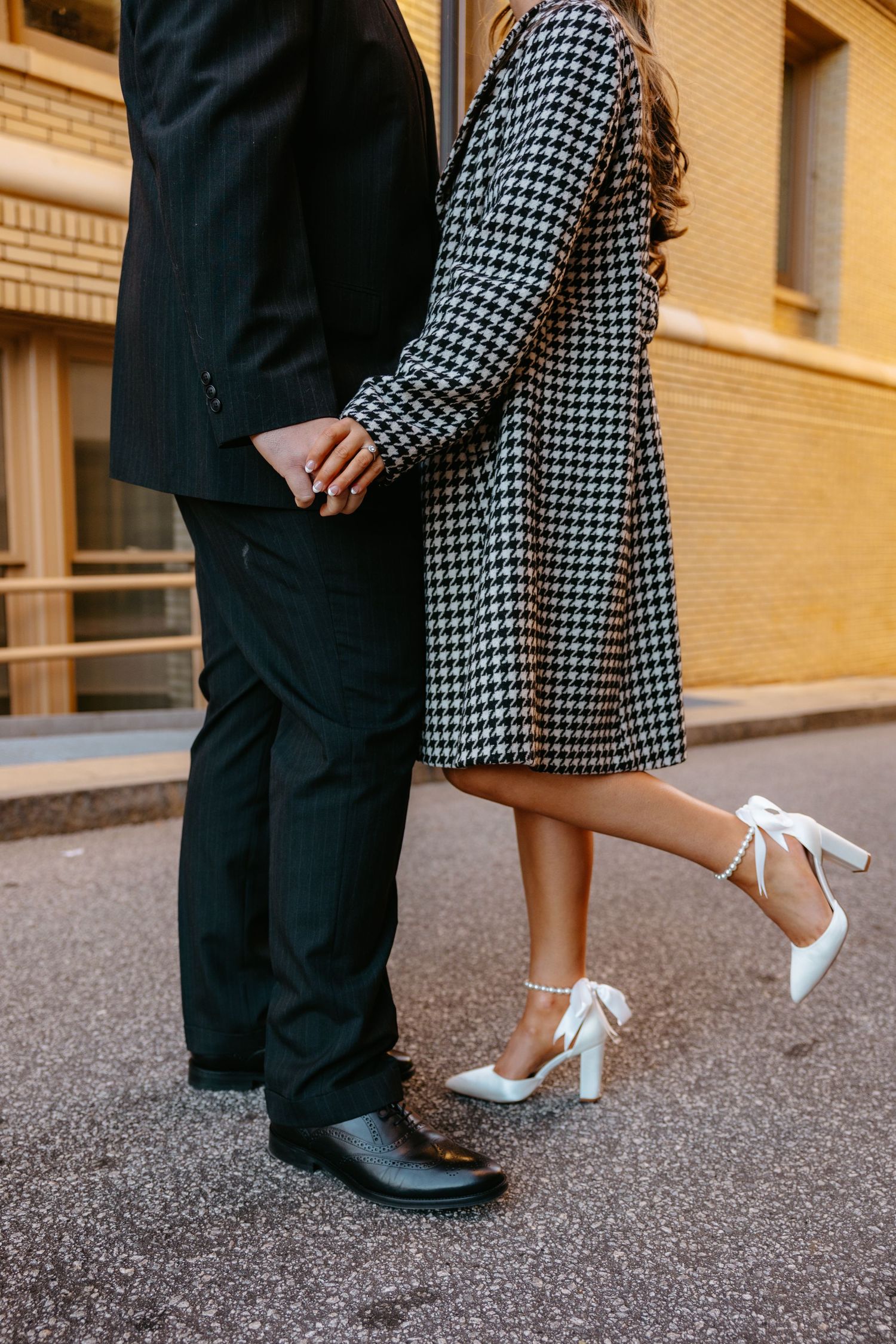 Close-up of couple's feet showing formal shoes and houndstooth dress against urban backdrop.