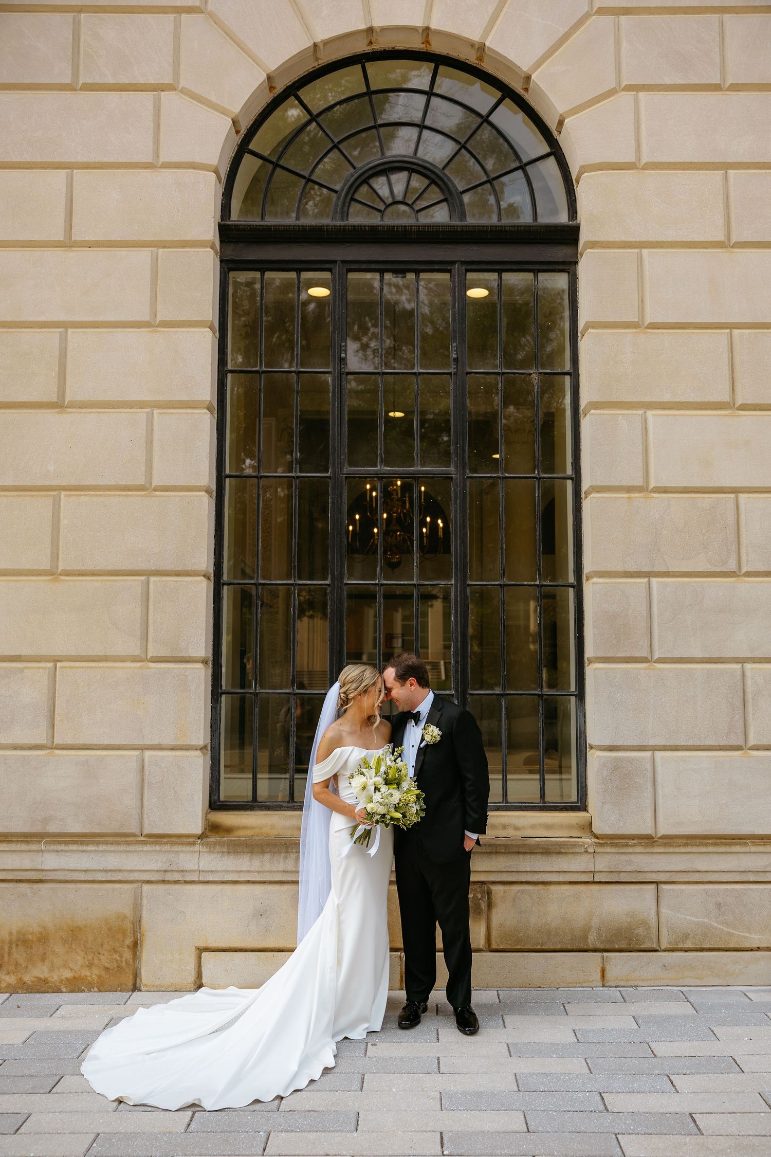 A wedding couple stands in an elegant sequence of four progressive shots against a stone building with arched windows.