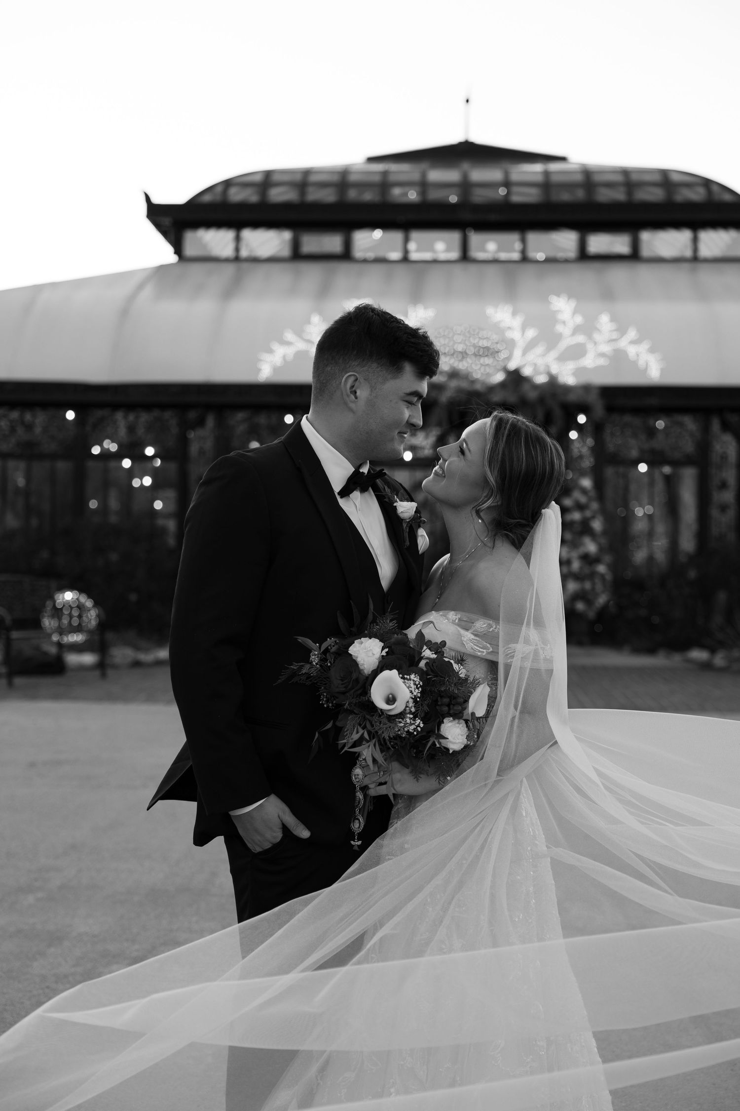A romantic black and white wedding photo series showing a couple sharing intimate moments with flowing veil outdoors.