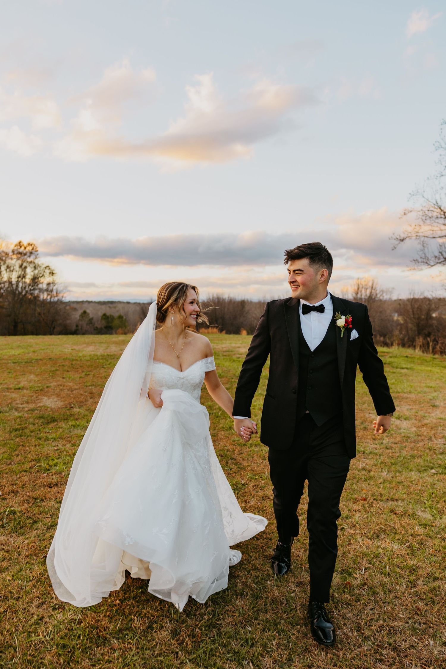 Newlyweds walking and laughing together in an open field during golden hour.