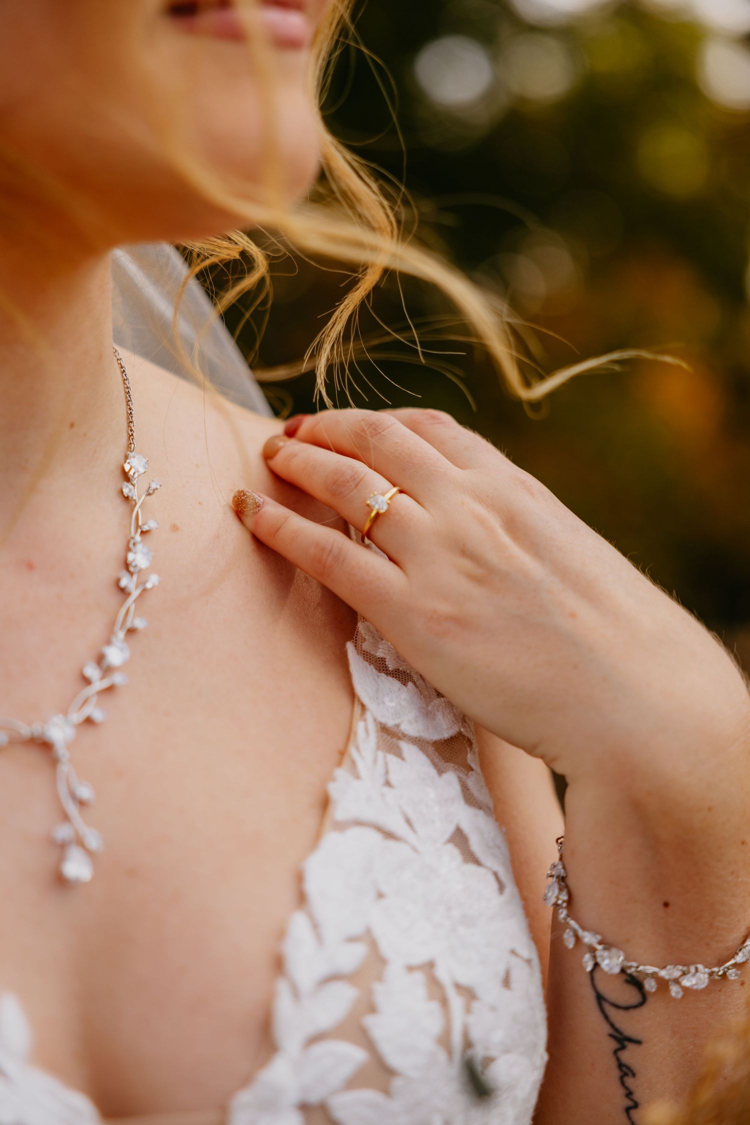 Close-up of delicate bridal jewelry and engagement ring with lace dress detail.